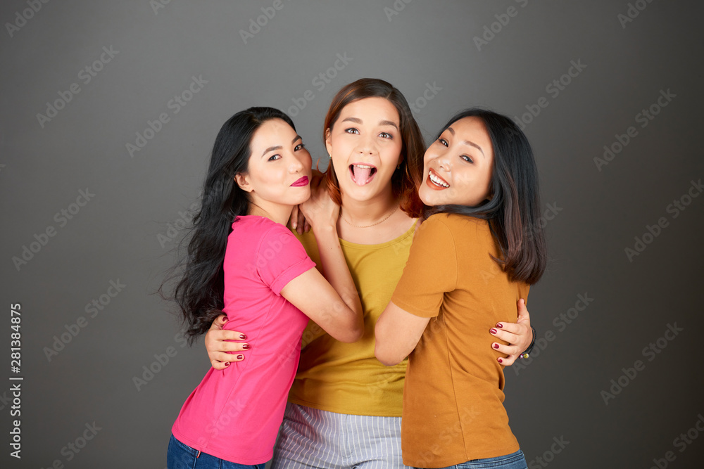 Portrait of happy young friends embracing each other and posing at camera over grey background Portrait of happy young friends embracing each other and posing at camera over grey background