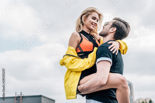 handsome man in glasses holding attractive woman in yellow jacket on roof
