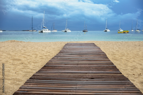 wooden walkway of a sandy beach against the background of the sea, white yachts and a cloudy sky