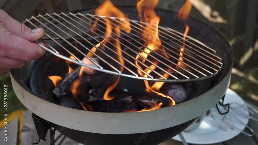 Metal barbeque grid getting put on by white male hands, while the bbq is really hot and flames are comming out. And correcting the metal grid with a spoon. Flaming in the charcoal. Metal barbeque grid getting put on by white male hands, while the bbq is really hot and flames are comming out. And correcting the metal grid with a spoon. Flaming in the charcoal.