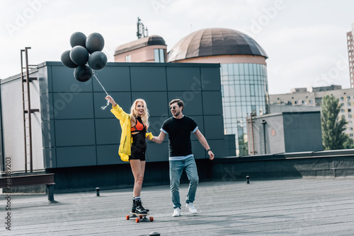 attractive woman with balloons skateboarding and man in glasses holding her hand © LIGHTFIELD STUDIOS