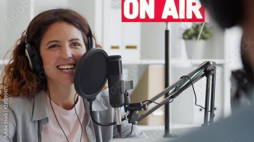 Back view of female Caucasian radio host with long curly hair sitting at mike, communicating cheerfully with man sitting in front of her photo