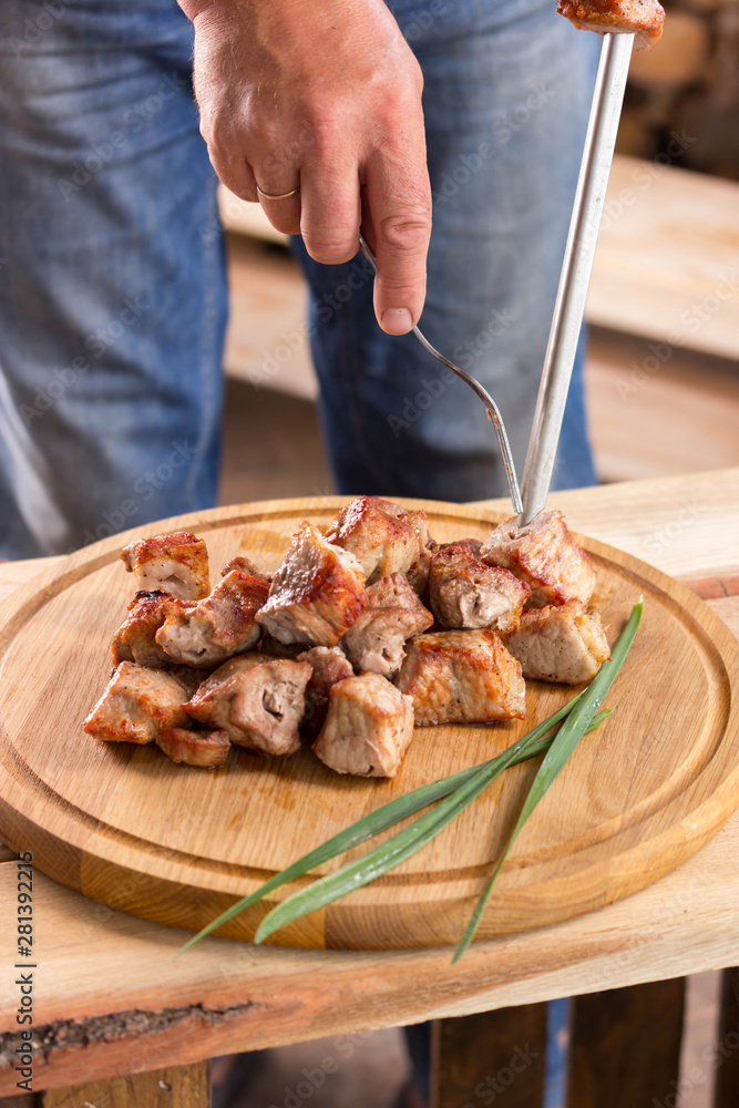 Man holds a round wooden board with pieces of fried meat and green onions