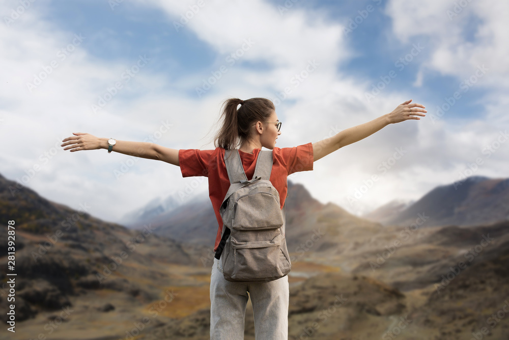 Woman traveler with a backpack, holding up her hands, stands on the top of the mountain. The beauty of nature, snowy mountains. sky and clouds Woman traveler with a backpack, holding up her hands, stands on the top of the mountain. The beauty of nature, snowy mountains. sky and clouds