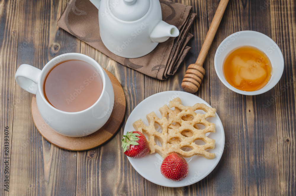 Delicious breakfast with tea, honey and wafers decorated with fresh strawberry on a wwoden table. Top view Delicious breakfast with tea, honey and wafers decorated with fresh strawberry on a wwoden table. Top view