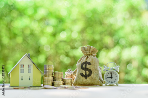 Mortgage-backed security MBS, financial concept : House model, stacks of rising coins, US dollar, money bags, a clock on a table over green background, depicts investment in home bought from the bank  photo