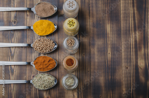Colourful various spices in spoons and in glass jars on a wooden table. Top view and copyspace. Cooking background.