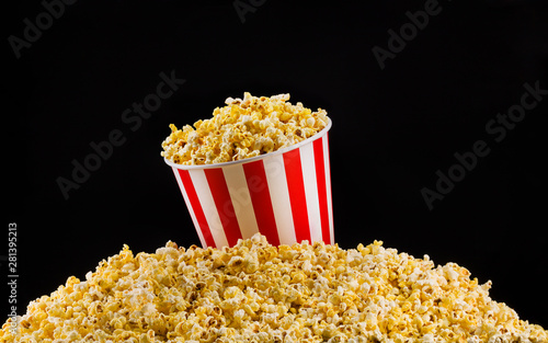 Paper striped bucket installed on scattered popcorn isolated on black background