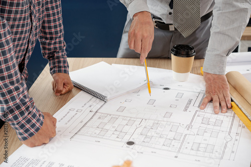 Close-up of businessmen pointing at construction blueprint drawing the sketches with pencils and developing new construction project at office