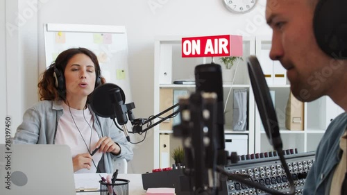 Rack focused shot of female radio host sitting at mike and having conversation with male guest sitting nearby photo