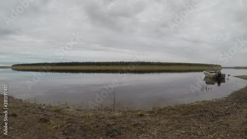 The movement of the taiga river the Vilyui ulus Suntar in Yakutia. Timelapse of water flow and cloudy sky on the shore on the background of mountains and coniferous forest and tied iron Soviet boat. photo