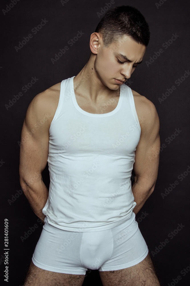 Muscle strong beautiful stripped male model in denim blue jeans with white t-shirt on grey isolated font background Muscle strong beautiful stripped male model in denim blue jeans with white t-shirt on grey isolated font background
