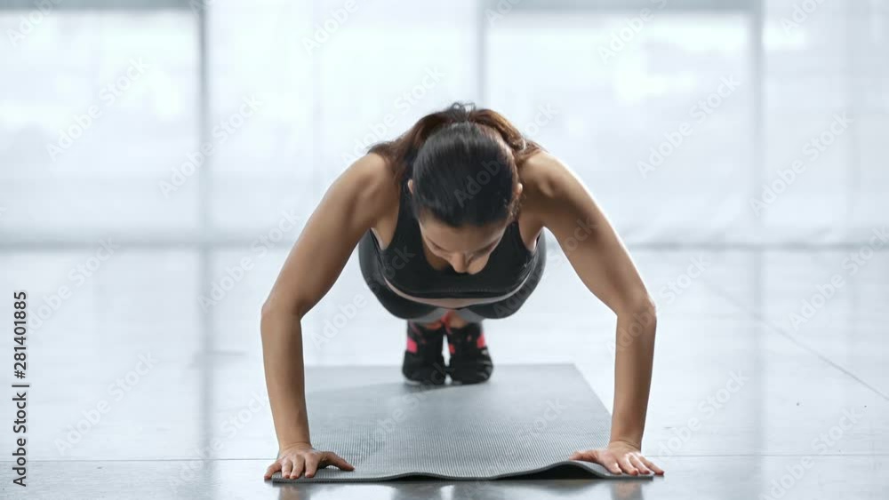 young sportswoman doing push ups on fitness mat in sports center