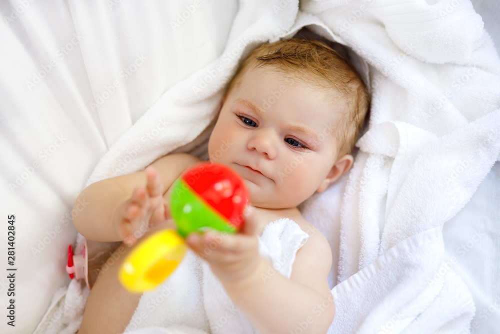 Cute little baby playing with toy rattle and own feet after taking bath. Adorable beautiful girl wrapped in white towels Cute little baby playing with toy rattle and own feet after taking bath. Adorable beautiful girl wrapped in white towels
