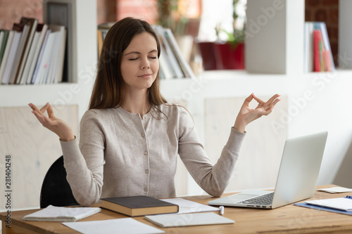 Peaceful girl distracted from studying meditating at workplace photo