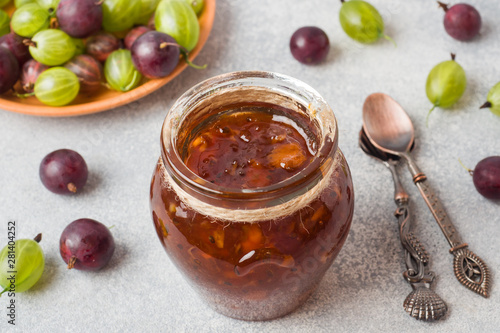 Gooseberry jam in a jar with fresh gooseberry berries on a gray background.