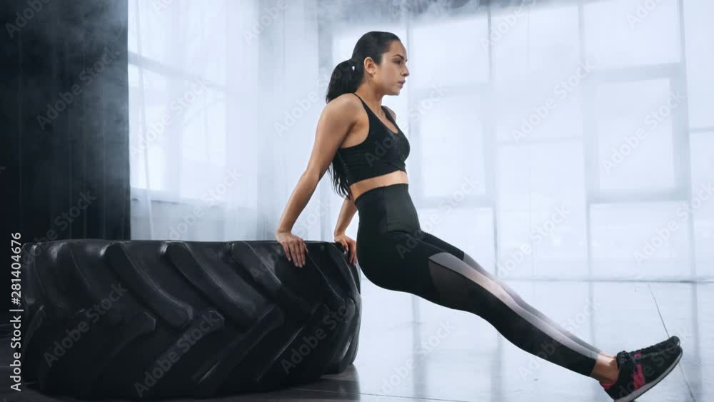 beautiful young sportswoman doing push ups on tire in sports center