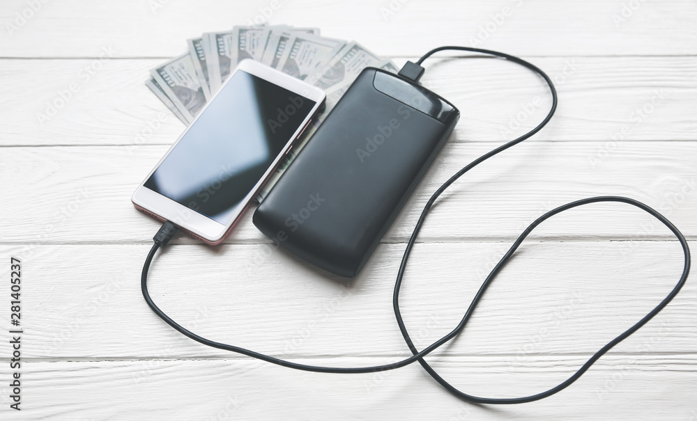 Black power bank with usb and smartphone on wooden background. Dollar notes lying nearby. Modern information technology photo. Black power bank with usb and smartphone on wooden background. Dollar notes lying nearby. Modern information technology photo.