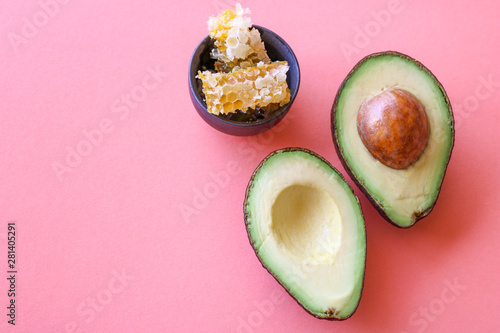 Avocado halves and a small bowl with honeycombs isolated on pink/coral background