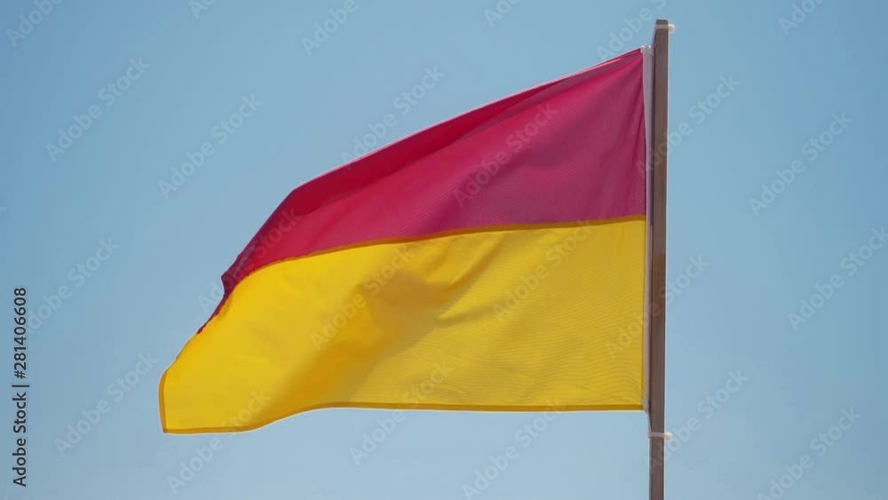 Red and yellow beach safety flag against pale sky. Red and yellow beach safety flag against pale sky.