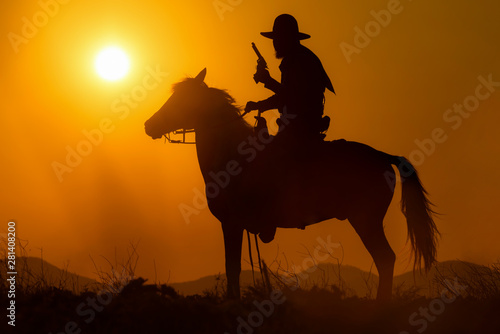 Cowboy riding a horse carrying a gun in sunset with mountain scene in Pakchong, Nakhonratchasima, Thailand
