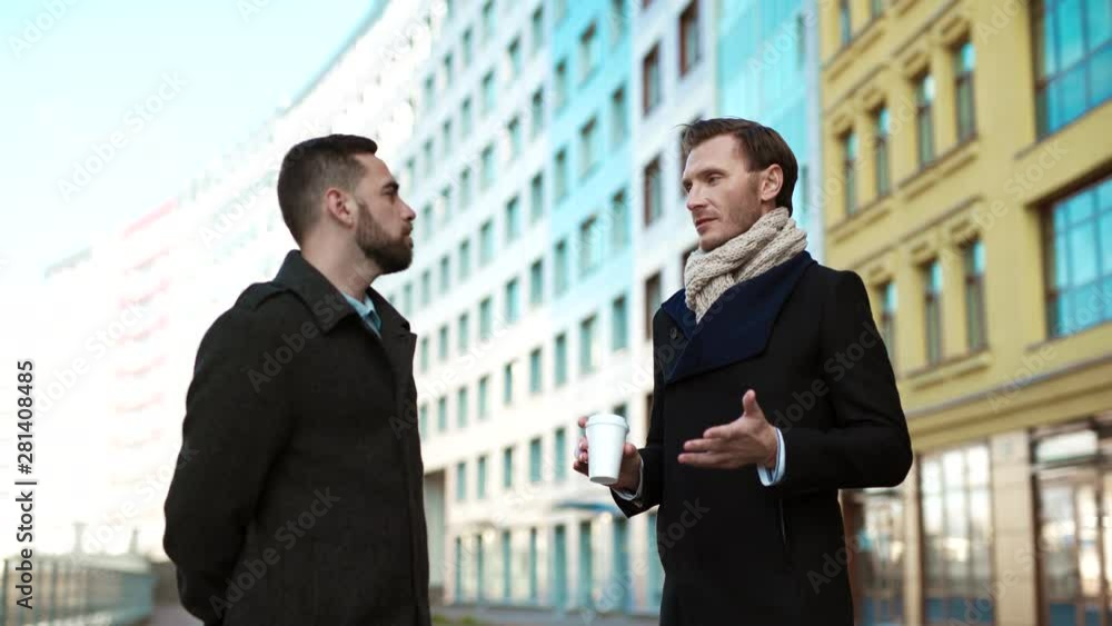 Medium shot of two male businessmen standing outdoors in front of each other and talking Medium shot of two male businessmen standing outdoors in front of each other and talking