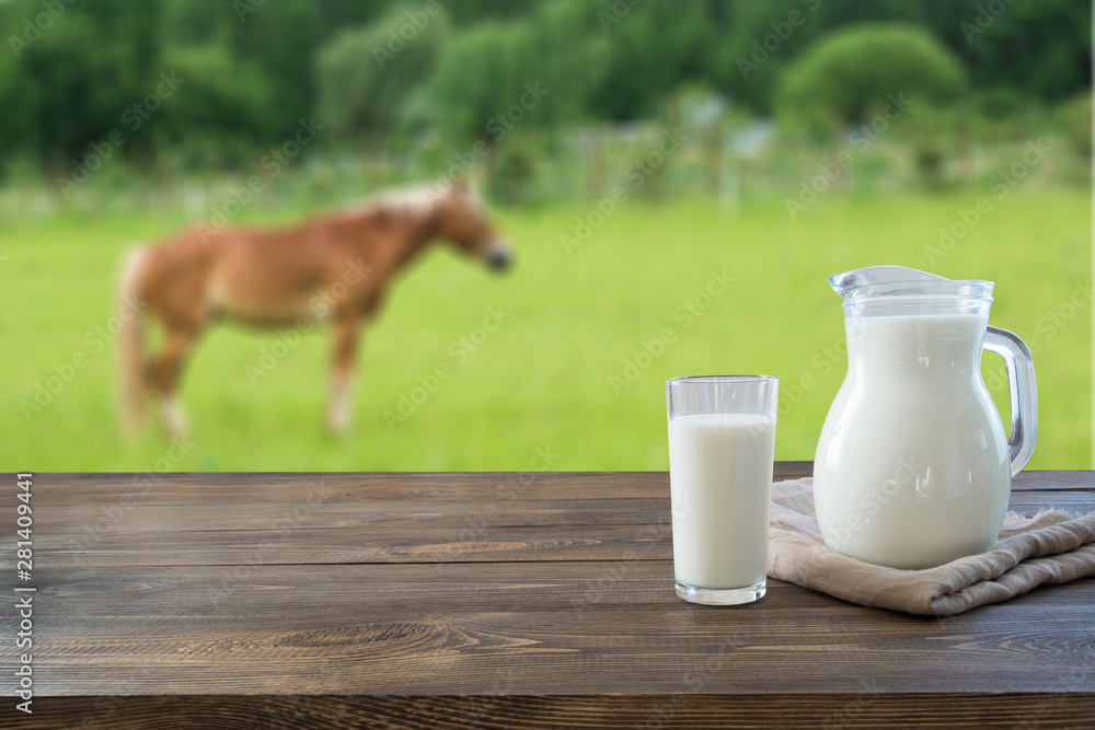 Fresh koumiss milk in glass on wooden table and blurred landscape with horse on green summer meadow.Healthy eating. Rustic style. Fresh koumiss milk in glass on wooden table and blurred landscape with horse on green summer meadow.Healthy eating. Rustic style.