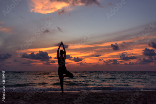 Silhouette of girl doing yoga on the beach during sunrise