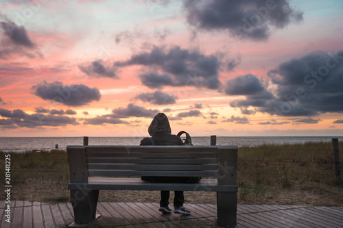 Jemand sitzt und schaut den Sonnenuntergang auf einer Sitzbank am Meer am Strand