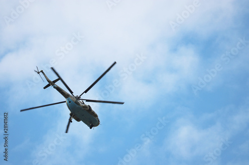 Military helicopter in flight on background of blue sky with white clouds. Bottom view, air forces concept