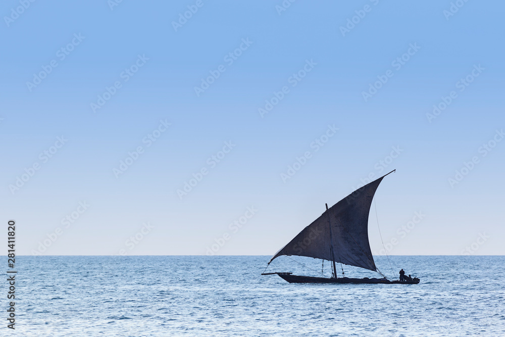 Traditional dhow sailing vessel used to transport people goods and commodities silhouetted against a blue coean and sky
