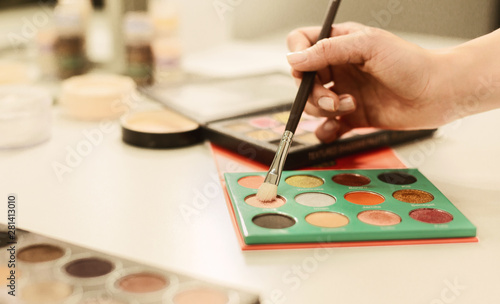 Makeup Artist Holding Brush And Eyeshadow Palettes Lying On Table