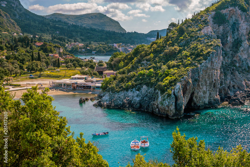 Beautiful landscape with sea–lagoon, beach, colorful boats on turquoise water surface, mountains and cliffs, green trees and bushes, blue sky and clouds. Corfu Island, Greece.  photo