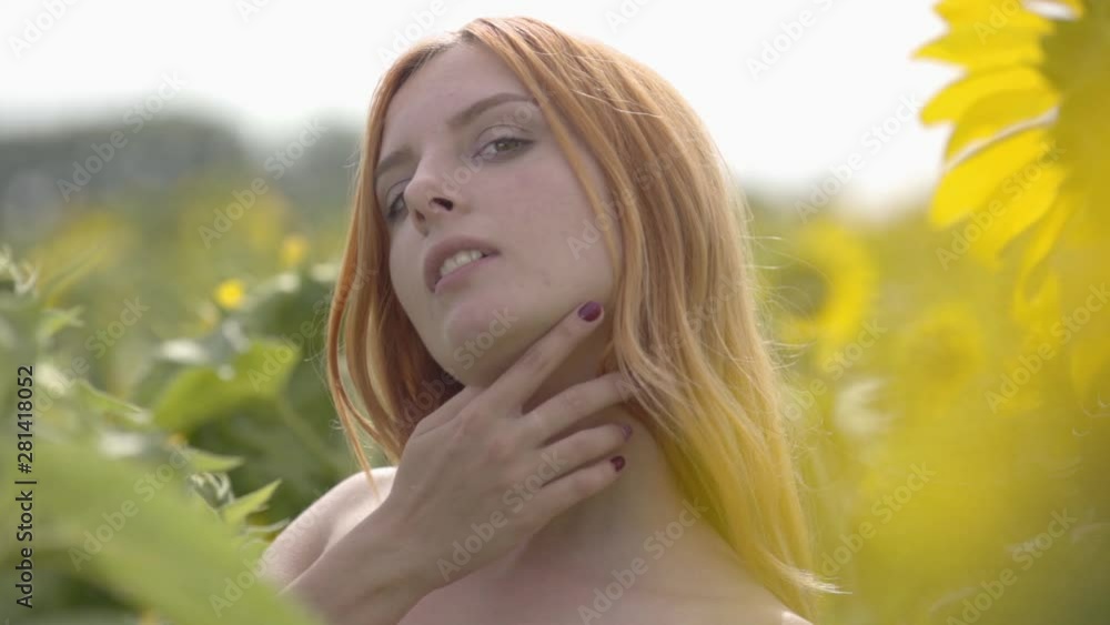 Portrait of cute confident sensual girl with red hair and green eyes standing on sunflower field. Concept of beauty, connection with nature. Freedom concept. Happy woman outdoors. Slow motion. Portrait of cute confident sensual girl with red hair and green eyes standing on sunflower field. Concept of beauty, connection with nature. Freedom concept. Happy woman outdoors. Slow motion.