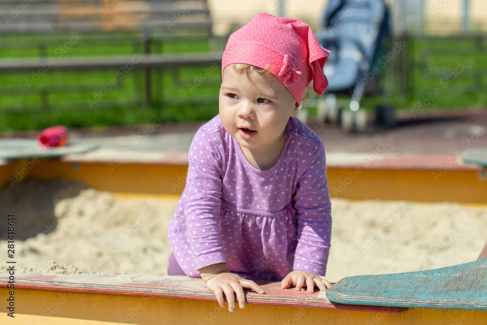 Little girl 1 year old in dress and scarf looks to the side cheerfully. horizontal close-up Little girl 1 year old in dress and scarf looks to the side cheerfully. horizontal close-up