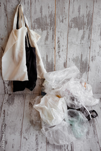 eco-friendly cotton shopping bags hanging vs many plastic bags on a rustic wooden background © nelladel