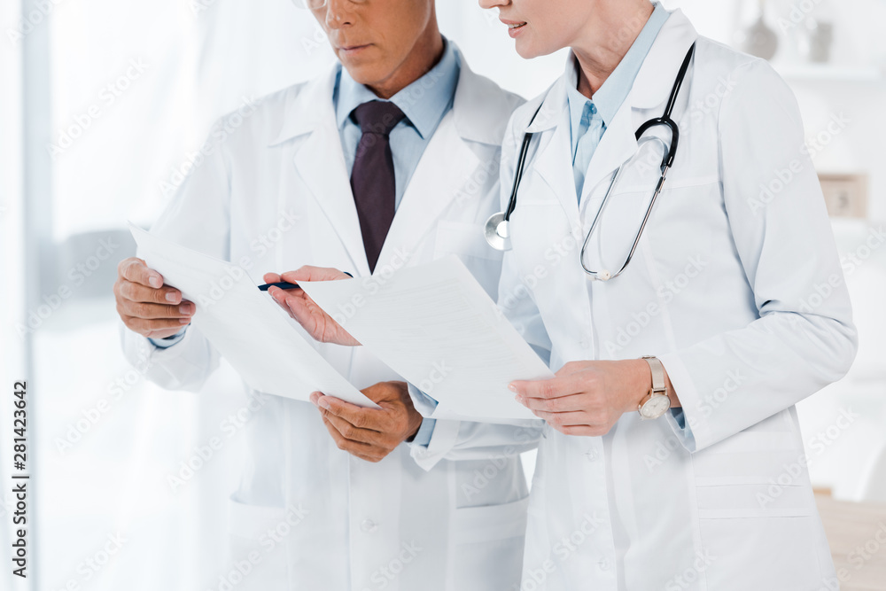 cropped view of doctors holding blank papers in clinic cropped view of doctors holding blank papers in clinic
