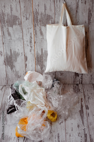 One eco-friendly cotton shopping bag hanging vs many plastic bags on a rustic wooden background © nelladel