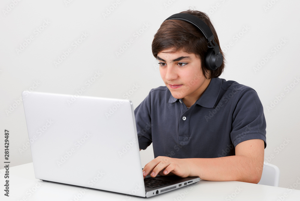 Gamer kid wears a wireless headphone and plays a computer game at his laptop computer Gamer kid wears a wireless headphone and plays a computer game at his laptop computer