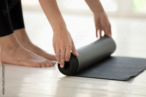 Sportswoman rolling black mat before or after yoga session