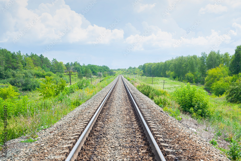 A railway through the summer green fields.  Beautiful green railway tree landscape sky clouds. Beautiful landscape. Railway transport.