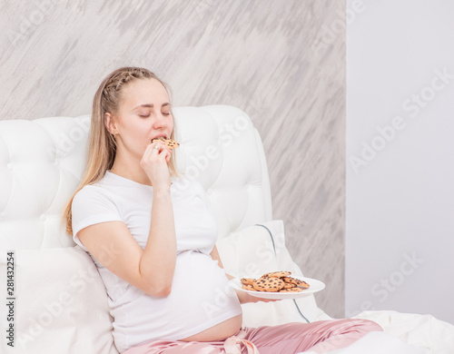 Happy pregnant woman with cookies on the bed. Empty space for text