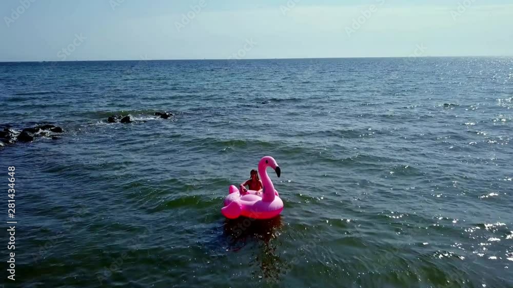 YOUNG BEAUTIFUL GIRL LIES ON RUBBER PELICAN, FLAMINGO BOAT IN THE WATER ON THE BEACH YOUNG BEAUTIFUL GIRL LIES ON RUBBER PELICAN, FLAMINGO BOAT IN THE WATER ON THE BEACH