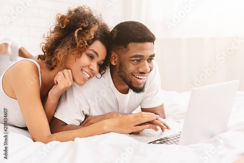 Young black couple lying on bed and using laptop