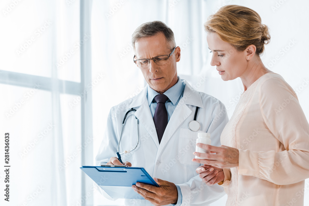 doctor in glasses holding clipboard with pen near woman with bottle doctor in glasses holding clipboard with pen near woman with bottle