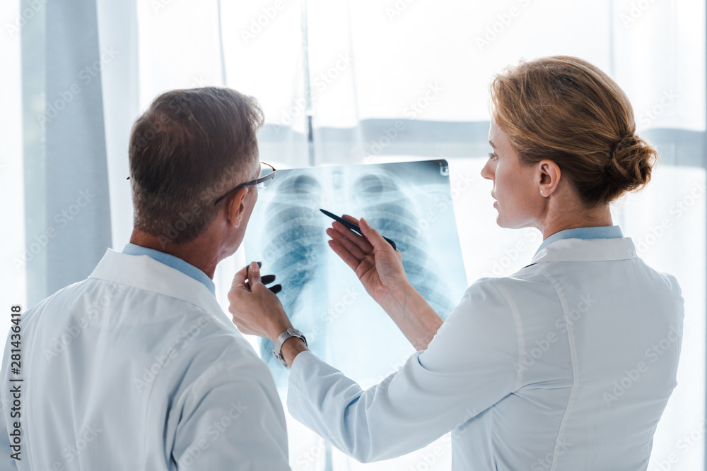 Obraz premium attractive doctor holding pen and x-ray near coworker