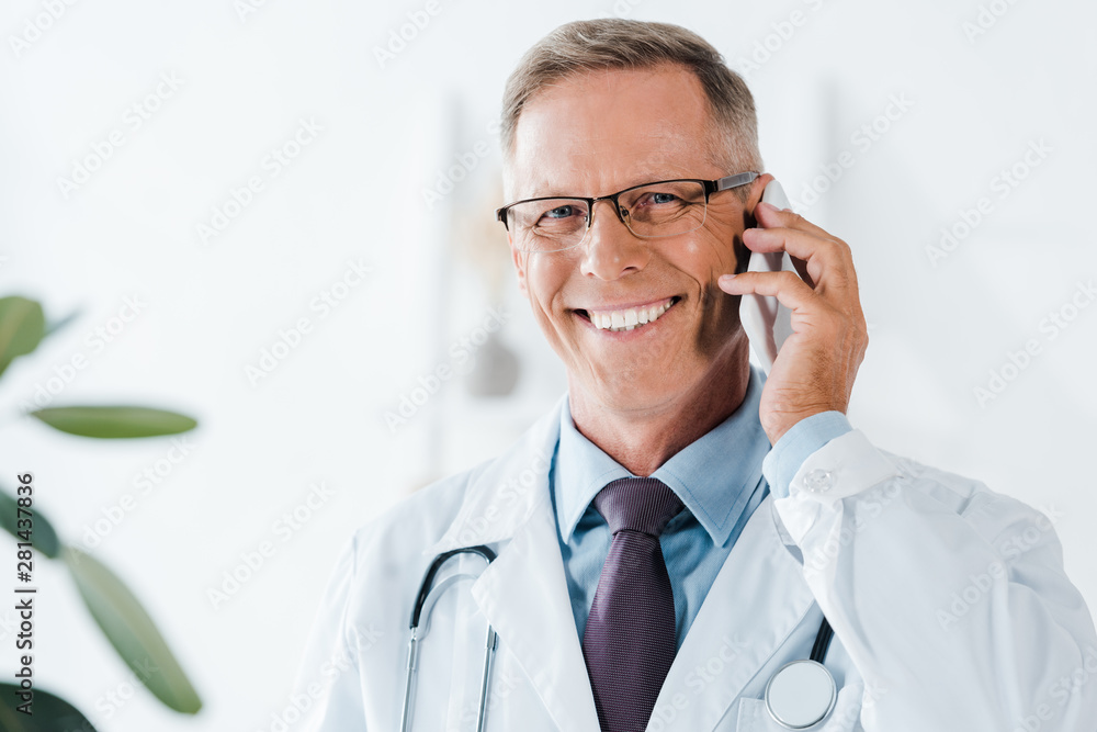 happy doctor looking at camera and talking on smartphone in clinic happy doctor looking at camera and talking on smartphone in clinic