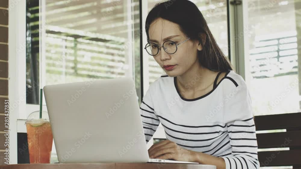 Young Asian woman working on freelance from home typing email on a laptop, girl using a computer for study online in coffee shop female user busy on a distance internet job. Young Asian woman working on freelance from home typing email on a laptop, girl using a computer for study online in coffee shop female user busy on a distance internet job.