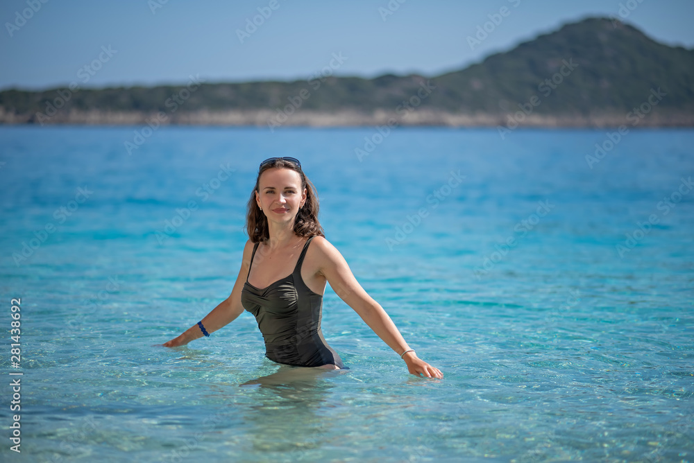 the beautiful woman in a price-work bathing suit costs on a belt in transparent blue water at the sea