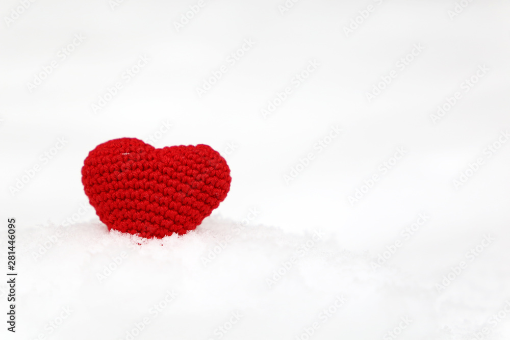 Red knitted heart on the snow, symbol of love with snowflakes. Background for Christmas holiday, Valentine's day greeting card, concept of romantic celebration